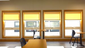 Interior view of a modular building featuring large windows with yellow shades, showcasing a workspace that emphasizes the benefits of permanent modular construction.