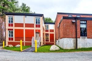 Triumph modular building featuring a combination of modern and traditional design elements in a modular construction setting. The image showcases the entrance and exterior of a permanent modular building with a landscaped area.